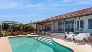 Une piscine avec une terrasse carrelée, des chaises longues blanches et un espace patio couvert.