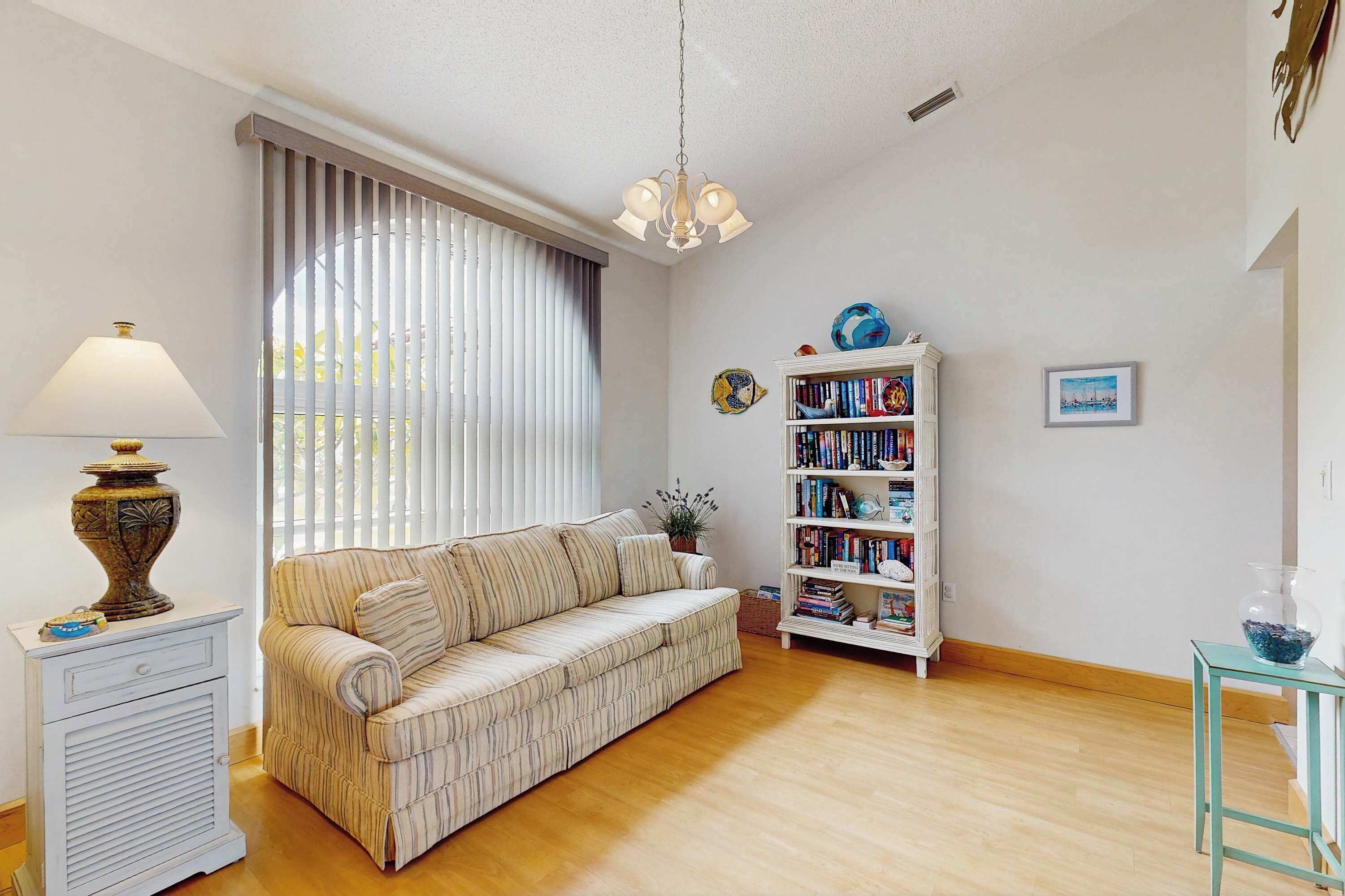 A living room with a sofa, a bookshelf, a lamp, and a window with blinds.