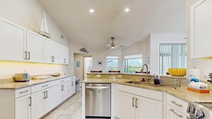 Une cuisine moderne avec des armoires blanches, un lave-vaisselle, un four encastré et un ventilateur de plafond.