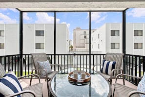 A balcony with a glass table, wicker chairs, and a tray with cups.