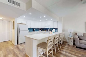 A modern kitchen with white cabinets, a central island with bar stools, a refrigerator, and a microwave. - Beachfront condo with pool, private balcony, and washer and dryer (Englewood)