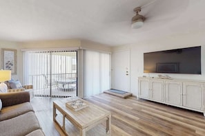 A living room with a sofa, coffee table, TV, and a sliding glass door leading to a balcony. - Beachfront condo with pool, private balcony, and washer and dryer (Englewood)