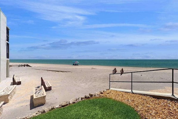 A beach view with a building, outdoor seating, and a railing. - Beachfront condo with pool, private balcony, and washer and dryer (Englewood)