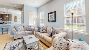 A living room with a sofa set, a coffee table, a floor lamp, and a kitchen area in the background. - Water-view condo with screened patio, pool, central AC, & private washer/dryer (Fort Myers)