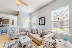 A living room with a sofa set, a coffee table, a floor lamp, and a kitchen area in the background. - Water-view condo with screened patio, pool, central AC, & private washer/dryer (Fort Myers)