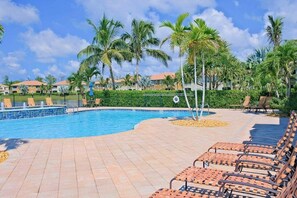 A swimming pool with lounge chairs, palm trees, and a fenced area. - Water-view condo with screened patio, pool, central AC, & private washer/dryer (Fort Myers)