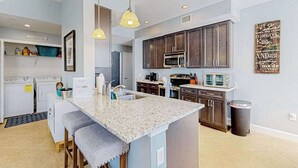 A modern kitchen with granite countertops, dark wooden cabinets, a built-in microwave, and a large island with bar stools. - Water-view condo with screened patio, pool, central AC, & private washer/dryer (Fort Myers)