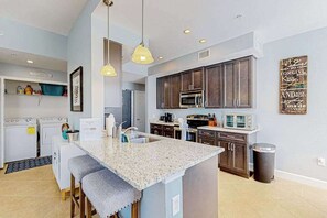 A modern kitchen with granite countertops, dark wooden cabinets, a built-in microwave, and a large island with bar stools. - Water-view condo with screened patio, pool, central AC, & private washer/dryer (Fort Myers)