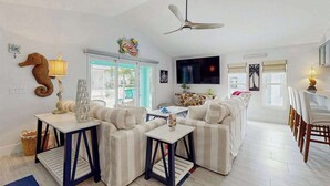 A living room with a sofa, two side tables, a ceiling fan, a television, and a dining area with chairs. - Single-story home with private yard, AC, & W/D - walk to beach, & dog-friendly (Englewood)
