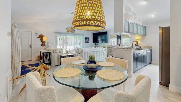 A modern dining area with a glass table, white chairs, a central decorative bowl, and a unique yellow pendant light. - Single-story home with private yard, AC, & W/D - walk to beach, & dog-friendly (Englewood)