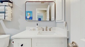 Un baño con tocador blanco, lavamanos, espejo y toallero con toallas dobladas.