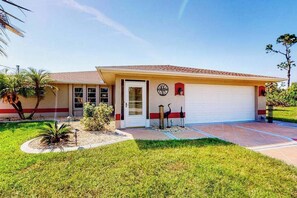 A single-story house with a garage, a front door, and a small garden area with a palm tree and shrubs. - Snowbird-friendly home with private pool, water views, patio & sunroom (Englewood)