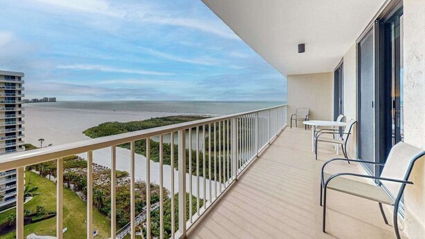 Een balkon met uitzicht op zee, een hekwerk en een paar stoelen.