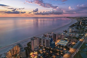 A coastal cityscape with a beachfront hotel, high-rise buildings, and a well-lit urban area. - Waterfront penthouse with beach views, pool, hot tub, & tennis court (Fort Myers Beach)