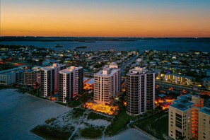 A coastal cityscape at dusk with high-rise buildings, a beach, and a marina. - Waterfront penthouse with beach views, pool, hot tub, & tennis court (Fort Myers Beach)