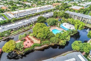 An aerial view of a hotel with a swimming pool surrounded by lush greenery and a small island with a red-roofed structure. - Spacious, waterfront condo with outdoor pool, tennis, & volleyball (Naples)