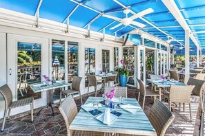 An outdoor dining area with tables and chairs, a blue canopy, and potted plants. - Spacious, waterfront condo with outdoor pool, tennis, & volleyball (Naples)