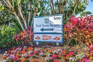 A sign for Park Shore Resort with an entrance arrow, surrounded by colorful flowers and trees. - Spacious, waterfront condo with outdoor pool, tennis, & volleyball (Naples)