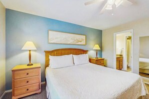 A bedroom with a bed, two bedside tables with lamps, a wooden headboard, a painting on the wall, and a door leading to another room. - Spacious, waterfront condo with outdoor pool, tennis, & volleyball (Naples)