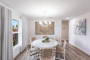 A dining area with a round table, white chairs, a chandelier, and a woven wall panel. - Exquisite home with private pool, washer & dryer, and internet (Marco Island)