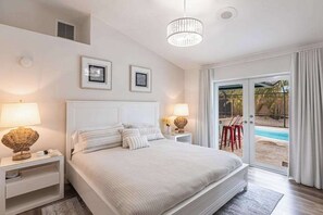 A bedroom with a bed, bedside tables, lamps, and a view of a pool through a sliding door. - Exquisite home with private pool, washer & dryer, and internet (Marco Island)