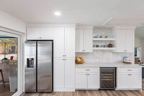 A modern kitchen with white cabinetry, a stainless steel refrigerator, a built-in oven, and a backsplash with hexagonal tiles. - Exquisite home with private pool, washer & dryer, and internet (Marco Island)