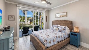 Un dormitorio con una cama grande, ventilador de techo, mesita de noche y vistas al exterior a través de un ventanal.