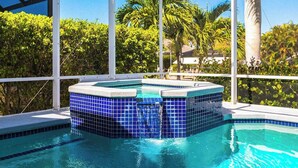 Una piscina con azulejos azules, un jacuzzi y vistas a palmeras.