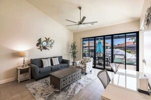 A living room with a sofa, coffee table, and a dining area with a table and chairs. - Modern waterfront retreat has pool with spa waterfall, close to Gulf beaches (Marco Island)