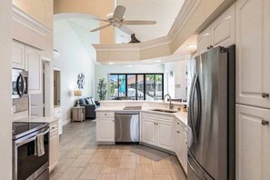A modern kitchen with a built-in dishwasher, a large refrigerator, and a ceiling fan. - Modern waterfront retreat has pool with spa waterfall, close to Gulf beaches (Marco Island)