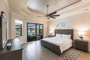 A bedroom with a bed, nightstands, a ceiling fan, and a view through a glass door. - Modern waterfront retreat has pool with spa waterfall, close to Gulf beaches (Marco Island)