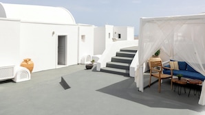 A white building with a staircase, a blue sofa, and a chair under a white canopy. - Hotiday Santorini Sea View (Santorini)