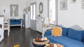 A modern living room with a blue sofa, a wooden coffee table with decorative items, a white dresser, and a bookshelf. - Hotiday Santorini Sea View (Santorini)