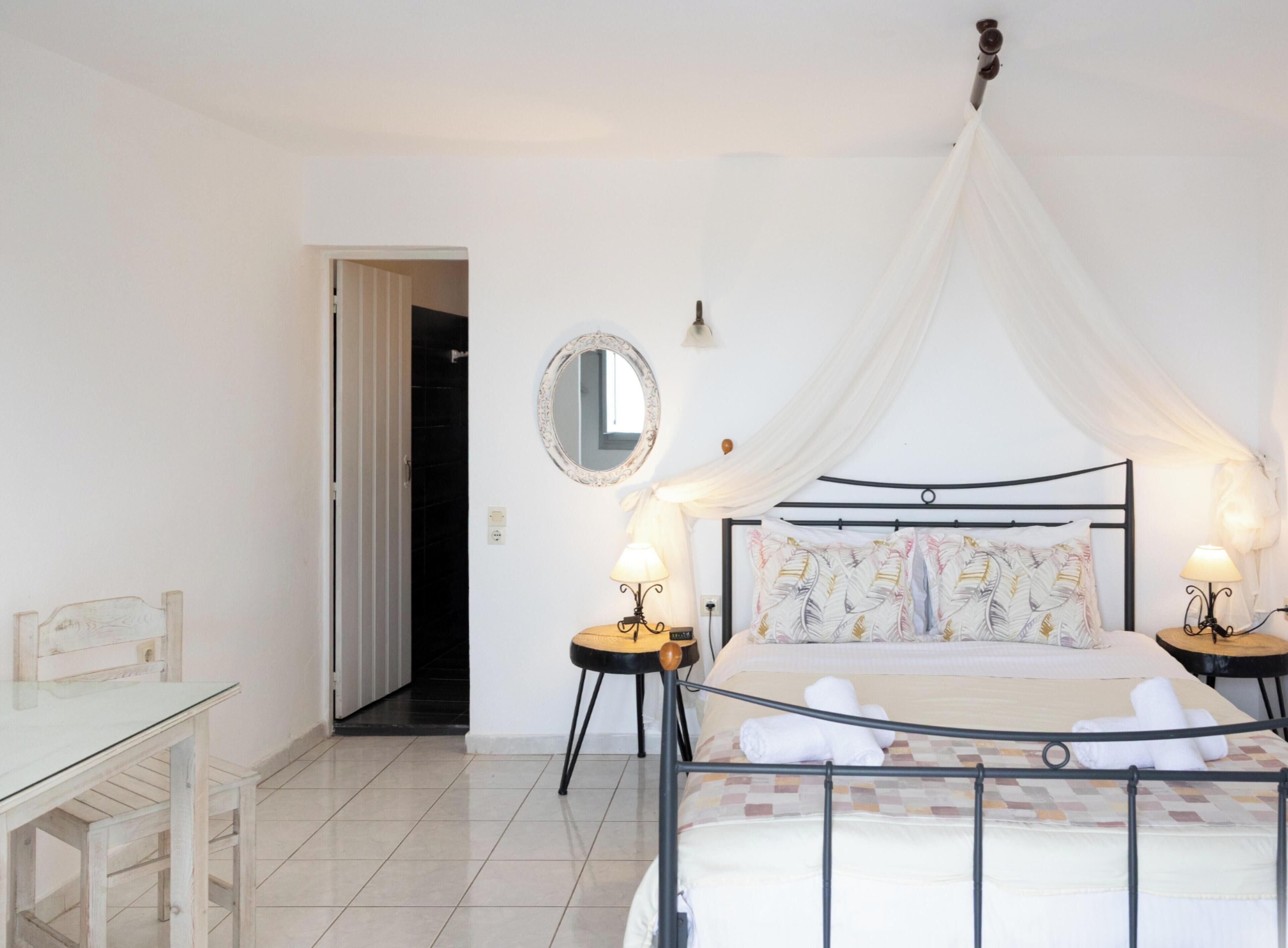 Un dormitorio con cama, mesitas de noche, un espejo y una puerta que da a otra habitación.