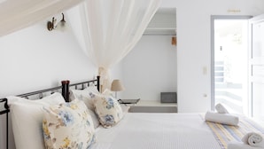 A bed with a canopy, a bedside table with a lamp, and a view of the outside. - Hotiday Santorini Sea View (Santorini)