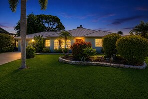 A residential house with a well-maintained lawn, a stone border, and a variety of plants. - Fantastic waterfront escape with hot tub, lanai, boat lift, WiFi & central AC (Bonita Springs)