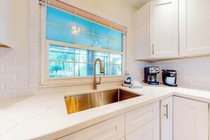 A kitchen with a large window, white cabinets, a stainless steel sink, and coffee makers. - Fantastic waterfront escape with hot tub, lanai, boat lift, WiFi & central AC (Bonita Springs)