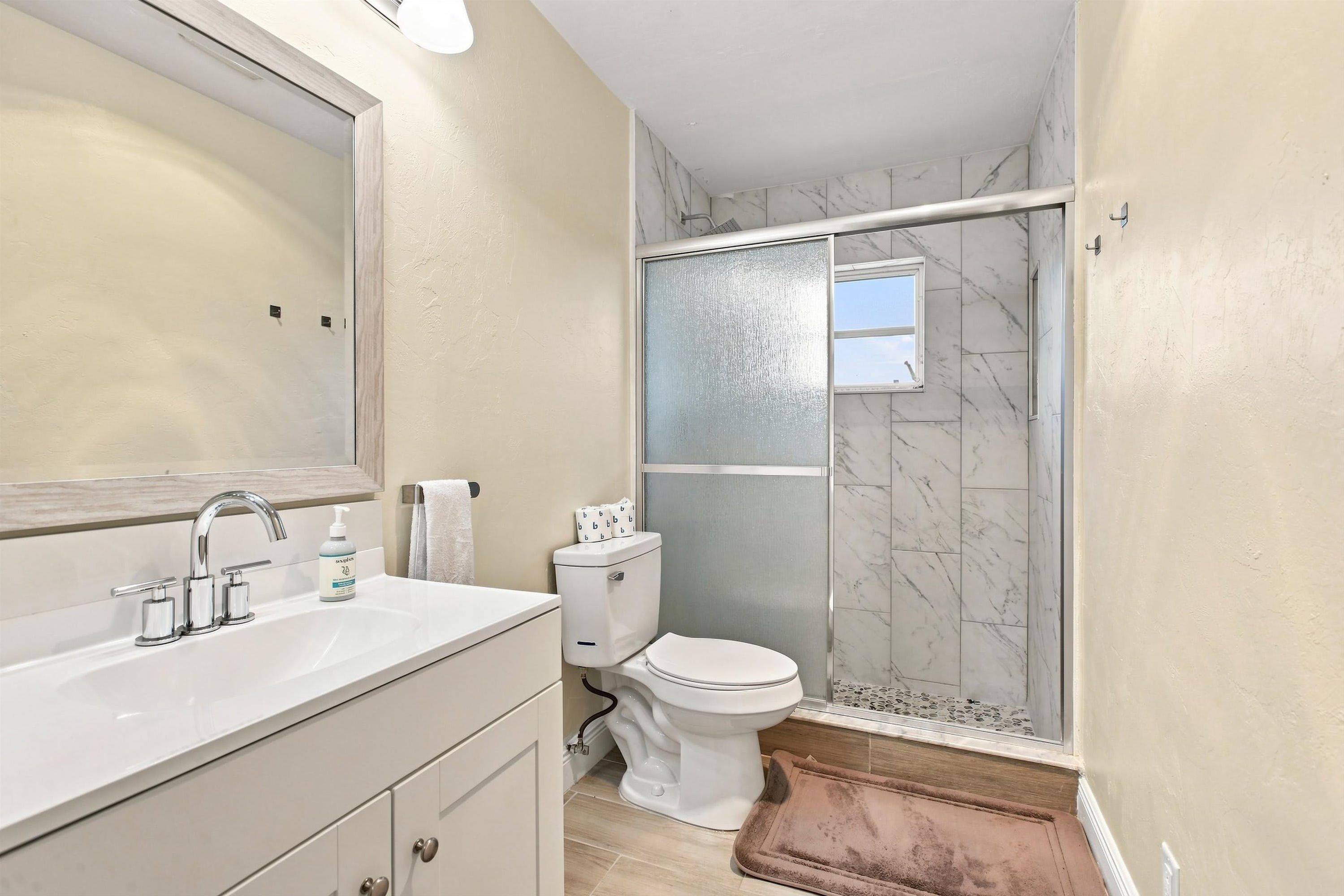 A bathroom with a large mirror, a sink, a toilet, and a shower enclosure.