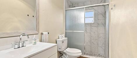 A bathroom with a large mirror, a sink, a toilet, and a shower enclosure.