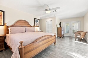 A bedroom with a wooden bed, a ceiling fan, a nightstand, a dresser, a chair, and a door leading to another room. - Fantastic waterfront escape with hot tub, lanai, boat lift, WiFi & central AC (Bonita Springs)
