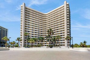 A multi-story hotel with a curved facade, balconies, and palm trees in the foreground. - Waterview condo with shared pool, panoramic balcony views, and WIFI (Marco Island)