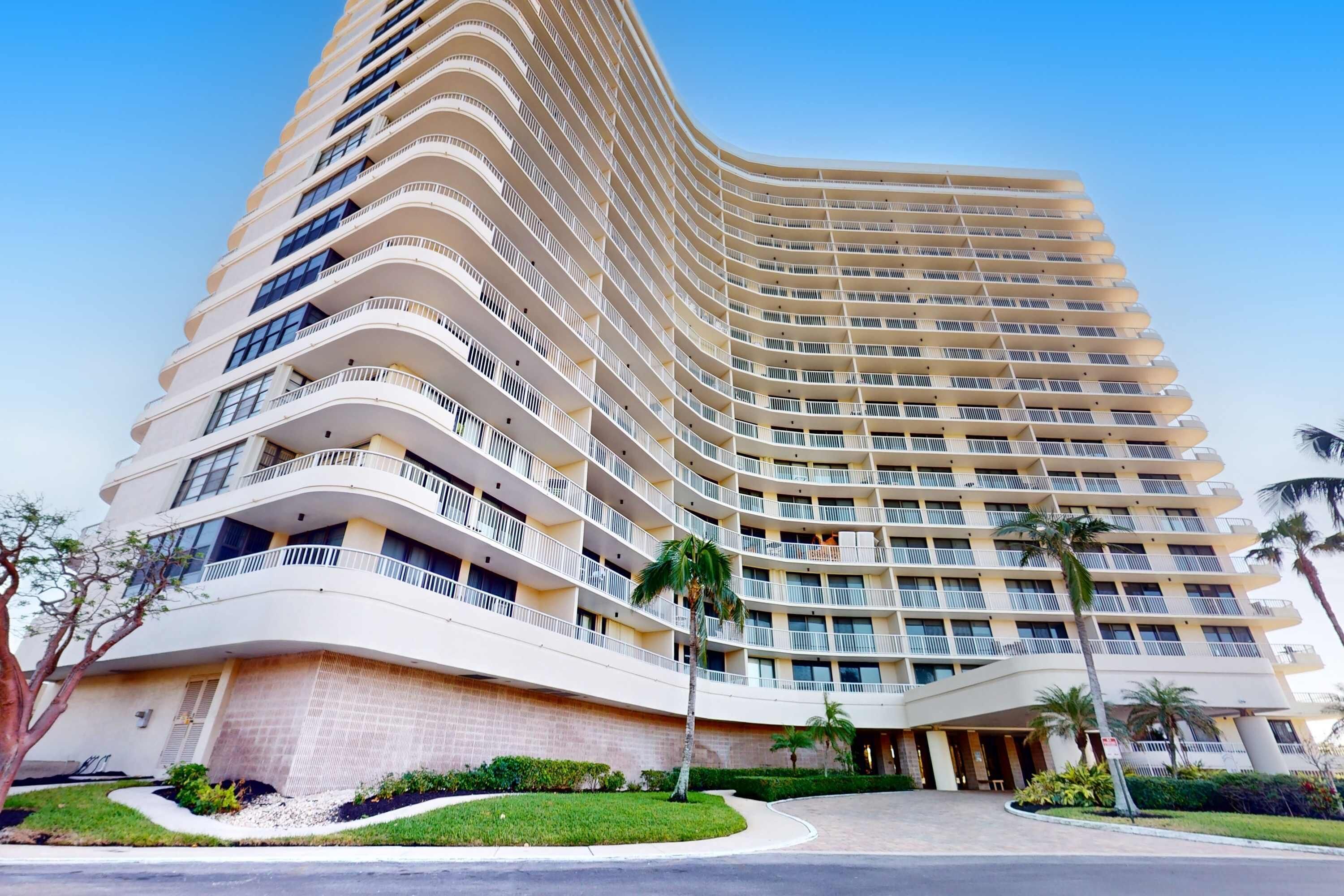 A multi-story hotel with balconies, a curved facade, and a landscaped entrance.