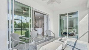 A balcony with wicker chairs and a table, large glass doors leading to a kitchen, and a ceiling fan. - Contemporary Getaway with an Enclosed Yard, Fast WiFi, & Furnished Lanai (Bonita Springs)