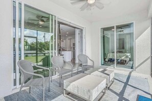 A balcony with wicker chairs and a table, large glass doors leading to a kitchen, and a ceiling fan. - Contemporary Getaway with an Enclosed Yard, Fast WiFi, & Furnished Lanai (Bonita Springs)