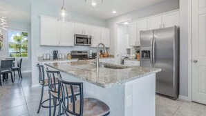 A modern kitchen with white cabinets, stainless steel appliances, a granite countertop island, and bar stools. - Contemporary Getaway with an Enclosed Yard, Fast WiFi, & Furnished Lanai (Bonita Springs)
