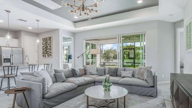 A modern living room with a sectional sofa, a round coffee table, and a dining area with a kitchen in the background. - Contemporary Getaway with an Enclosed Yard, Fast WiFi, & Furnished Lanai (Bonita Springs)