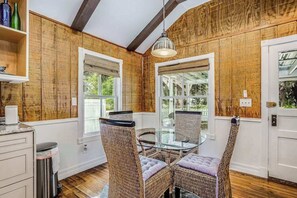 A dining area with wicker chairs, a glass table, and wooden walls. - Snowbird-friendly historical cottage with high-speed WiFi & washer/dryer (Bonita Springs)