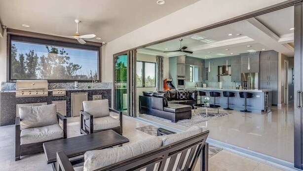 A modern kitchen with a large island, a dining area with a sofa and chairs, and a view through a glass door to a living room.
