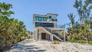 A modern two-story building with a balcony, a staircase, and a sandy foreground.