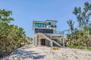 A modern two-story building with a balcony, a staircase, and a sandy foreground. - Spacious modern home close to beach with pool, central AC, & washer/dryer (Bonita Springs)